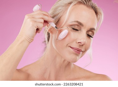 Face roller, beauty and woman facial massage with dermatology and cosmetic tools. Happy mature person on pink background for skincare, self care and rose quartz results for anti aging, glow and shine