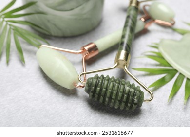 Face rollers, gua sha tool and palm leaves on gray background, closeup
