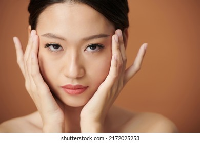 Face Of Serious Young Vietnamese Woman Touching Her Flawless Soft Skin And Looking At Camera