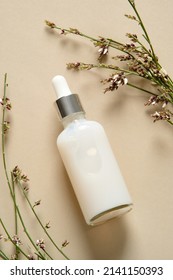 Face Serum Bottle With Flowers On Beige Background. Natural Cosmetics.