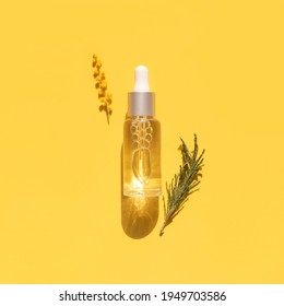 Face Serum In A Glass Bottle With A Pipette, Mimosa Flowers On Yellow Background Flat Lay Top View. Blank Label Package For Branding Mock-up. Spring Cosmetics Concept. Natural Organic Beauty Product