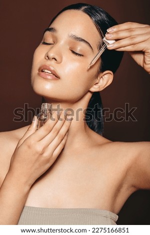 Face serum for a radiant complexion and flawless skin. Confident young woman dropping facial oil on her skin in a studio. Woman practicing skin care with moisturising beauty products.