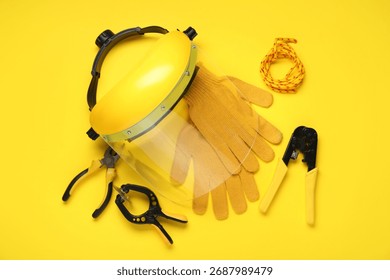 Face shield, gloves and construction tools on yellow background