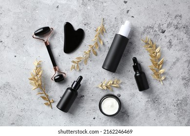 Face skin care concept. Obsidian stone face roller, gua sha, black dropper bottles with serum, moisturizer cream jar on concrete table. Flat lay, top view. - Shutterstock ID 2162246469