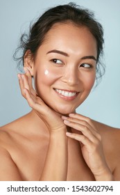 Face Skin Care. Woman Applying Cosmetic Cream On Clean Hydrated Skin Portrait. Beautiful Happy Smiling Asian Female Model With Natural Makeup Applying Facial Moisturizer, Beauty Product. High Quality