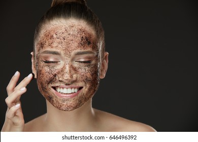 Face Skin Scrub. Portrait Of Sexy Smiling Female Model Applying Natural Coffee Mask, Face Scrub On Facial Skin. Closeup Of Beautiful Happy Woman With Face Covered With Beauty Product. High Resolution