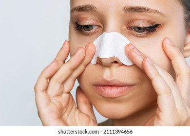 The face of a woman cleaning the skin of her nose with strips from blackheads or black dots isolated on a white background. Acne problem, comedones. Enlarged pores on the face. Cosmetology concept
