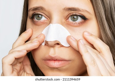 The face of a woman cleaning the skin of her nose with strips from blackheads or black dots isolated on a white background. Acne problem, comedones. Enlarged pores on the face. Cosmetology concept