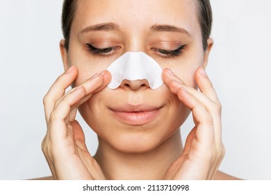 The face of a woman cleaning the skin of her nose with strips from blackheads or black dots and looking down isolated on a white background. Acne problem, comedones. Enlarged pores on the face 