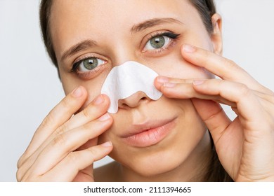The face of a woman cleans the skin of her nose using strips from blackheads or black dots isolated on a white background. Acne problem, comedones. Enlarged pores on the face. Cosmetology concept