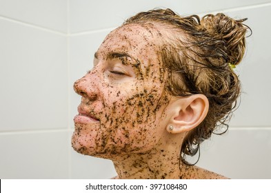 Face of a young beautiful girl on black coffee is deposited mask, taking a bath on the background of white tiles, naked with wet hair, enjoys the spa treatments for beauty and health