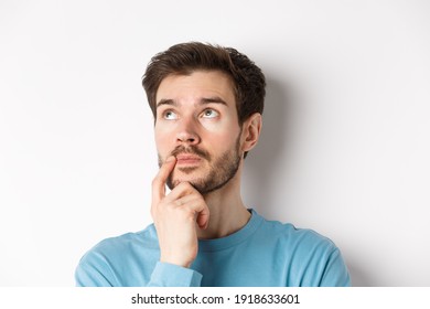 Face Of Young Caucasian Man Looking Up Pensive, Making Choice Or Thinking, Pondering While Standing Over White Background