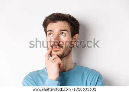 Face of young caucasian man looking up pensive, making choice or thinking, pondering while standing over white background