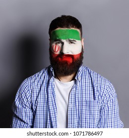 Face of young man painted with flag of Iran. Football or soccer team fan, sport event, faceart and patriotism concept. Studio shot at gray background, copy space