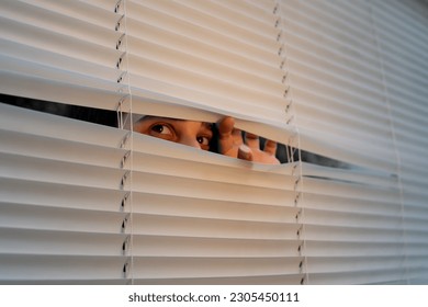 Face of young woman 22 years old, peering between white blinds. Close-up, peeping. - Powered by Shutterstock