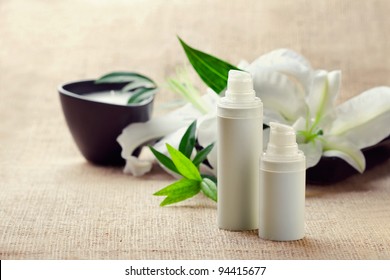 Face/body care concept: bottles of creams/lotions/serums with white lily flowers, closeup shot