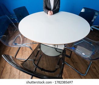 A faceless business woman in a suit sits alone at a round table in a meeting room. The female boss is waiting for her team in the boardroom.