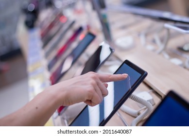 Faceless Caucasian Woman Chooses A Smartphone In An Electronics Store. Close-up Of A Female Hand With A Phone Tester