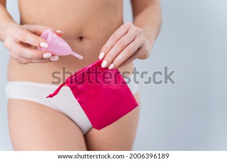 A faceless Caucasian woman in underpants puts a pink menstrual cup in a small silk bag. Eco Friendly Products: Feminine intimate hygiene during menstruation