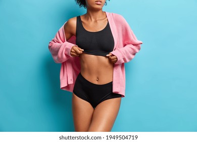 Faceless female model shows her beautiful fitness body dressed in underwear and pink jumper has slender legs and flat belly. Womans fit figure. Blue background