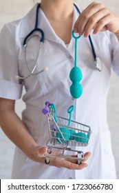 A Faceless Gynecologist Puts A Set Of Vaginal Balls Into A Miniature Shopping Cart. The Doctor Holds A Mini Trolley And Device For The Muscles Of The Pelvic Floor. Female Health Concept. Kegel Toy