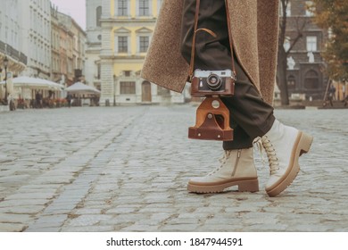 Faceless image of young stylish woman - travel blogger walking down the central city street using old-fashioned vintage camera. Autumn or spring outdoor fashion details, trendy street outfit