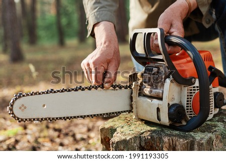 Faceless logger preparing chainsaw for work, cheking saw for faults, unknown logger forester with professional tool for cutting trees on background of forest.