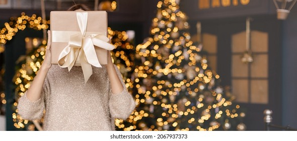 Faceless Man Holding A Box With A Christmas Present In His Hands. Gold Ribbon Gift Wrapping. New Year Bokeh Background Copyspace Place For Text. Festive Interior