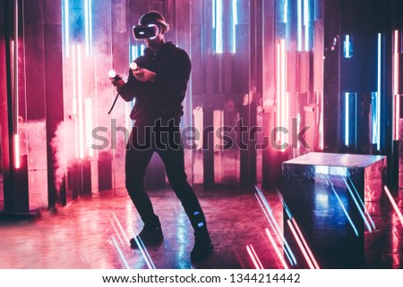Faceless man wearing VR headset in dark space with neon light lamps, user turning head side to looking virtual reality, shoting through colored flares and bokeh on foreground