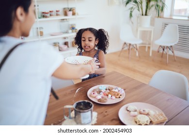 Faceless Mother Giving Strainer To Concentrated Little Black Kid With Dirty Face And Curly Pigtails During Cooking On Big Kitchen Blurred Background