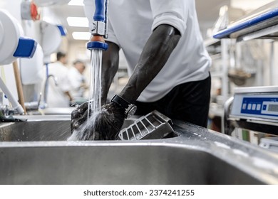 Faceless photo of the hands of an African man working in a restaurant kitchen as a cleaner - Powered by Shutterstock