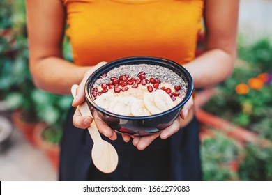 Faceless photo of a woman holding acai smoothie bowl with pomegranate and chia seeds and a wooden spoon - Powered by Shutterstock