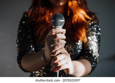 Faceless portrait of redhead woman in sparkly evening dress holding microphone on dark night background. Unrecognizable female singer with modern microphone in hands - Powered by Shutterstock