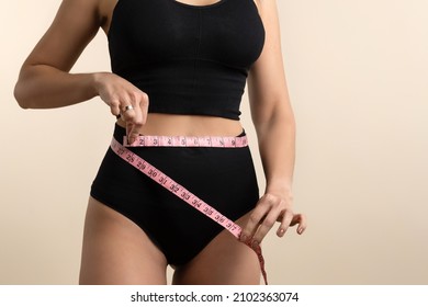 Faceless slim girl in black underwear with one-inch measuring tape at waist. Incognizable Fit Woman poses in high waist panties and top. Perfect female body. Diet or body care concept. Flat belly