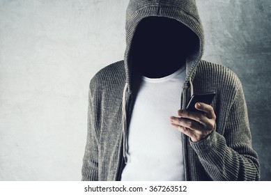 Faceless unrecognizable hooded person using mobile phone, identity theft and technology crime concept, selective focus on body