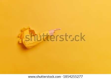Faceless woman breaks arm through paper yellow wall indicates on right at blank space gives advice to buy subscription suggests to click on link shows direction. Place for your advertisement