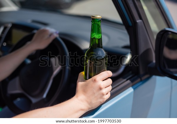 A\
faceless woman is drinking a bottle of beer while driving a car.\
Breaking the law and drinking alcohol while\
driving