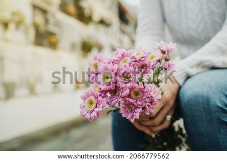 Faceless woman with flowers bouquet in hands sitting in cemetery
