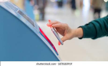 A faceless woman scans the qr code from her smartphone. A girl uses a self-service machine at the airport to check in for a flight and print tickets