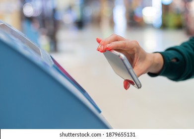 A faceless woman scans the qr code from her smartphone. A girl uses a self-service machine at the airport to check in for a flight and print tickets