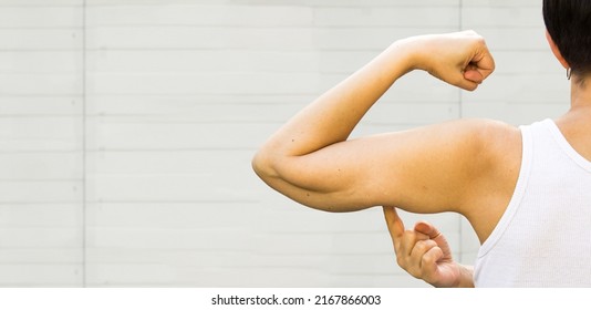 A Faceless  Woman Shows The Flabby Muscles Of The Arm With Her Index Finger. Flabby Arm Syndrome (FAS). Effect Of Aging Caused By Loss Of Elasticity And Muscle. Banner, Copyspace.