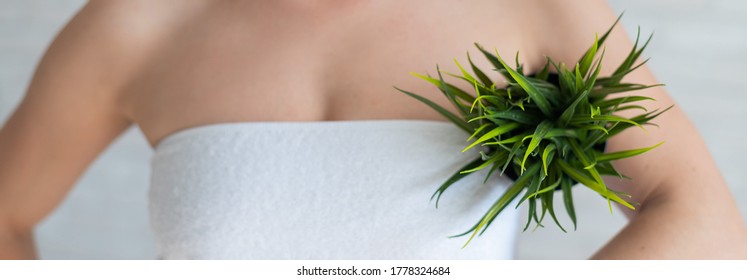 Faceless woman in a white towel holds a pot with a plant. Unrecognizable girl with the help of green bushes imitates the vegetation of armpit hair. Depilation area. Female hair removal.