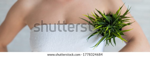 Faceless woman in a white towel holds a pot with\
a plant. Unrecognizable girl with the help of green bushes imitates\
the vegetation of armpit hair. Depilation area. Female hair\
removal.