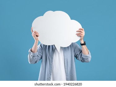 Faceless young man covering his face with speech bubble on blue studio background, mockup for design