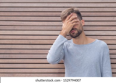 Facepalm. Ashamed Embarrassed Man Covering His Face. Young Guy On Wooden Wall Background With Copy Space. Emotion Facial Expression And Feelings Concept