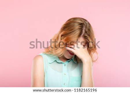 facepalm embarrassment and shame emotion. ashamed smiling girl covering her face with a hand. young beautiful woman portrait on pink background.