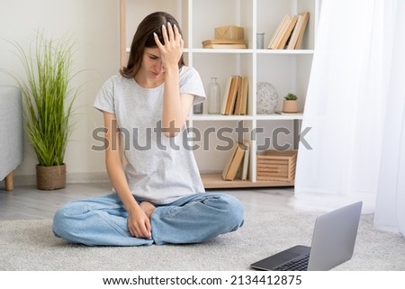 Facepalm gesture. Confused woman. Home education. Embarassed casual woman covering forehead with hand sitting floor with laptop light room interior.