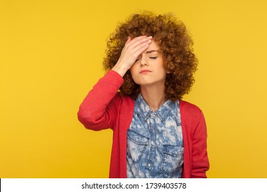 Facepalm. Portrait of depressed woman with curly hair slapping forehead in regret gesture, blaming herself, feeling shame and sorrow, body language. indoor studio shot isolated on yellow background