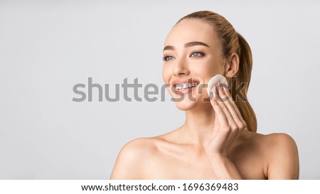 Facial Beauty Treatment. Happy Young Lady Using Cotton Pad Cleaning Face Looking Aside Over Gray Studio Background. Panorama, Free Space
