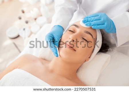 Facial Care. Cosmetologist Using Cotton Pads, Cleansing Skin Of Young Indian Woman During Beauty Treatments In Salon, Relaxed Hindu Female Lying On Table With Closed Eyes, Enjoying Skincare Procedure